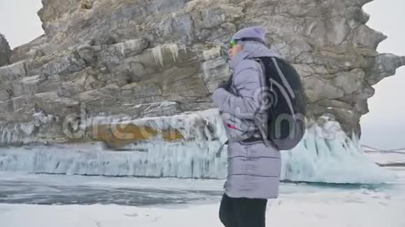 贝加尔湖冰上女子旅行去冬岛旅行女孩走在冰岩脚下旅行者看着视频的预览图