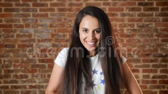 年轻漂亮的女孩微笑着看着镜头背景上的砖墙肖像视频的预览图