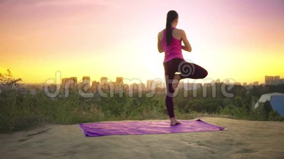 一个年轻的女人在大城市的背景下在山上练习瑜伽健康的女人在日落时做运动A视频的预览图