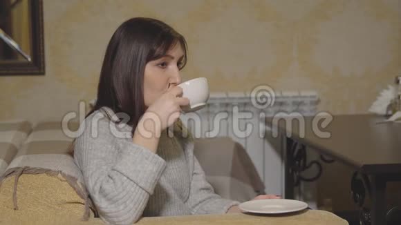 在咖啡馆里喝着白色杯子里的咖啡的年轻女人视频的预览图