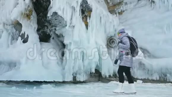 贝加尔湖冰上女子旅行去冬岛旅行女孩走在冰岩脚下旅行者看着视频的预览图