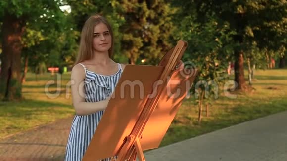 美丽的女孩在公园里画一幅画用颜料和铲子调色板带有图片的简易帆布视频的预览图