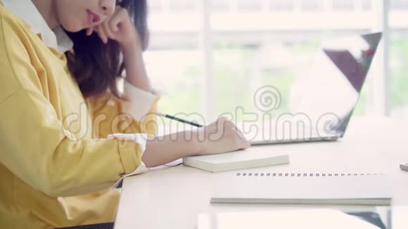 美丽的年轻微笑的亚洲女人在家客厅的桌子上工作笔记本电脑视频的预览图