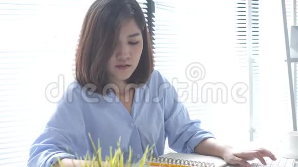 美丽的年轻微笑的亚洲女人在家里坐在客厅里用笔记本电脑工作视频的预览图