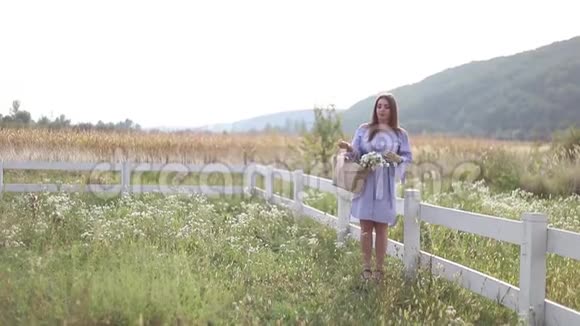 美丽的孕妇穿着蓝色的裙子走着听到农场的声音带花束的针织包树的背景视频的预览图