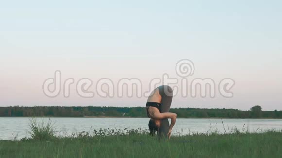 年轻的女孩在蓝色瑜伽垫上安静的风景做瑜伽的女人视频的预览图