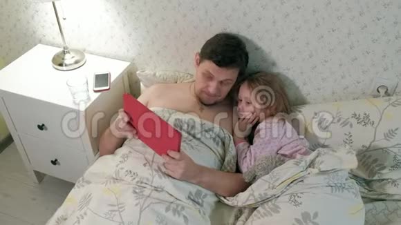 爸爸和小女儿在床上玩平板电脑视频的预览图