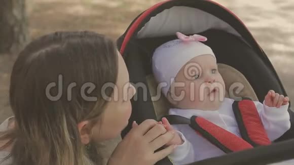 美丽的女人和她的小女儿散步推着婴儿车在公园里视频的预览图
