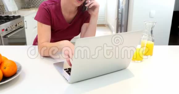 漂亮的女人在使用4k笔记本电脑时用手机说话视频的预览图