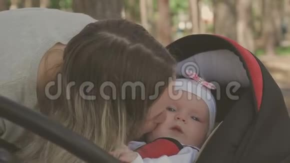 美丽的女人和她的小女儿散步推着婴儿车在公园里视频的预览图
