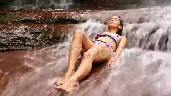 穿比基尼的女孩躺在瀑布河里视频的预览图