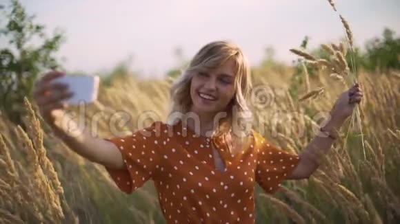 迷人的有趣的嬉皮士的金发女人在日落时在田野里用花束自拍视频的预览图