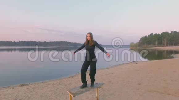 年轻漂亮的女孩穿着黑色衣服跳舞在河畔俯视风景视频的预览图