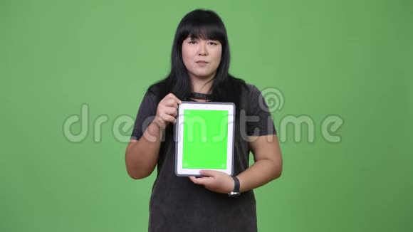 快乐超重的亚洲女人展示数码平板电脑视频的预览图