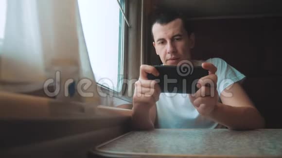 带智能手机的男商人乘火车旅行男旅行者正在铁路上的火车上输入网络信息视频的预览图