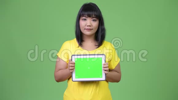 美丽快乐的亚洲女人展示数码平板电脑视频的预览图