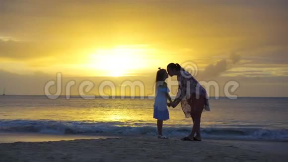 小女孩和快乐的母亲在海滩夕阳下的剪影视频的预览图