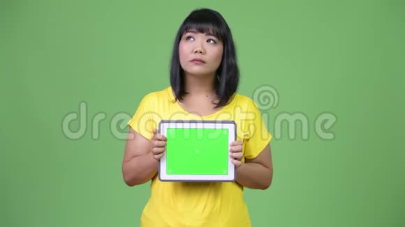 美丽的亚洲女人一边思考一边展示数码平板电脑视频的预览图
