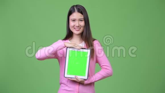 年轻美丽的亚洲女人展示数码平板电脑视频的预览图