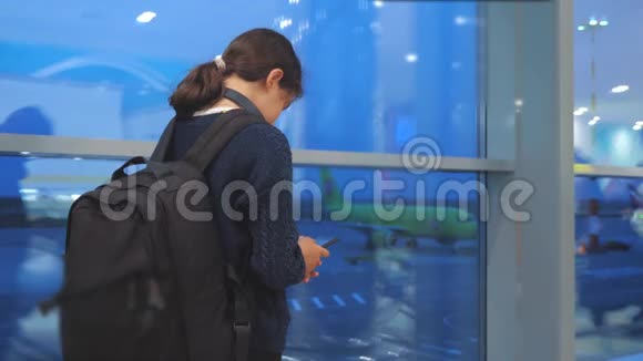 女儿旅行者带背包飞机航班机场概念带着智能手机的少女望着窗外视频的预览图