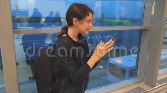 女儿带背包飞机飞行机场概念带着智能手机的少女望着窗外视频的预览图