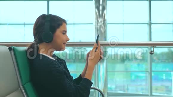 机场候机厅房间的生活方式为飞机航班戴着耳机听音乐的年轻快乐少女视频的预览图