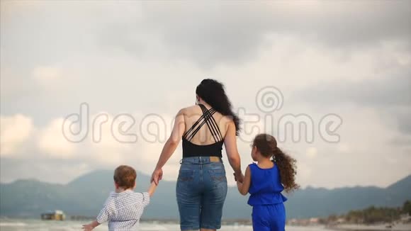 年轻的家庭母亲和孩子正沿着海岸散步幸福的家庭在海边散步视频的预览图