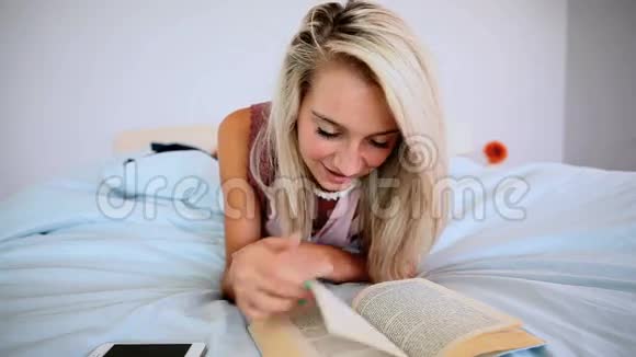漂亮的金发女郎躺在床上看书视频的预览图