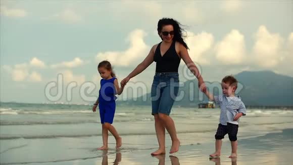 年轻的家庭母亲和孩子正沿着海岸散步幸福的家庭在海边散步视频的预览图