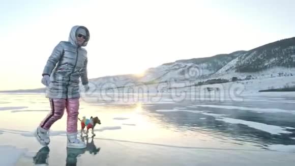 玩具猎犬穿着滑稽的衣服和滑稽的鞋子在漂亮的冰缝里玩球妈妈和女儿参加体育运动视频的预览图