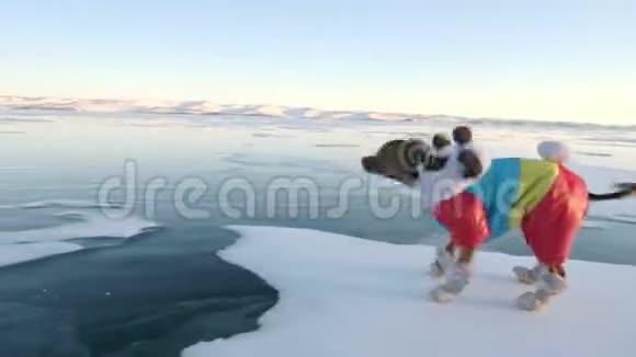 玩具猎犬穿着滑稽的衣服和滑稽的鞋子在漂亮的冰缝里玩球妈妈和女儿参加体育运动视频的预览图