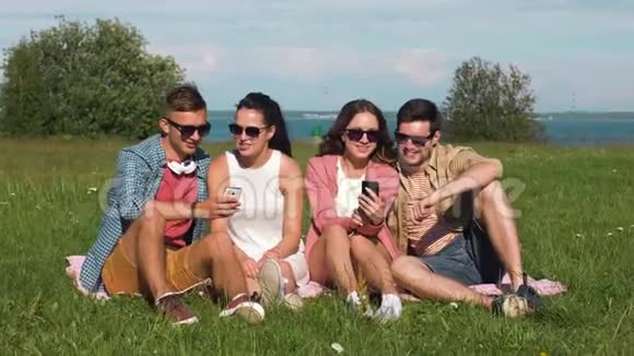 用智能手机微笑的朋友坐在草地上视频的预览图