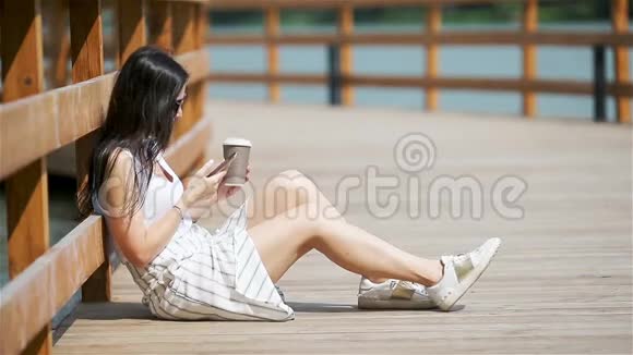 可爱的女人坐在公园里一边用手机看短信视频的预览图