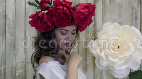 在镜头前摆姿势的女孩年轻的女人头上戴着一个猩红牡丹花圈一头乌黑的长发卷曲着视频的预览图