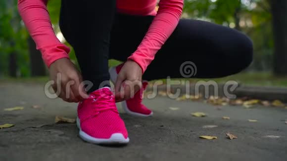 跑鞋日落时分女人系鞋带穿过秋天公园视频的预览图
