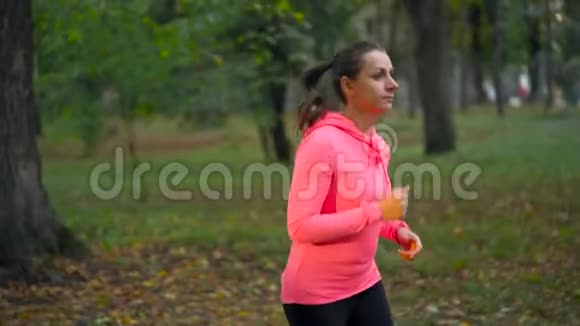 日落时分一个女人穿过一个秋天的公园慢动作视频的预览图