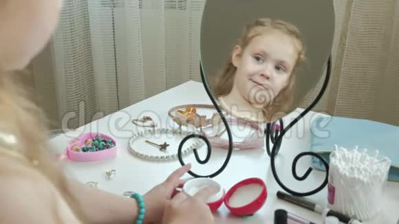 小女孩用红色的头发涂抹奶油照镜子化妆面部时尚时尚时尚化妆品在镜子中反射视频的预览图