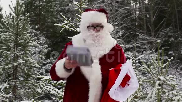 圣诞老人在白雪皑皑的树林里带着礼品盒视频的预览图