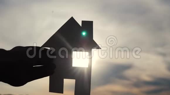 幸福家园建设理念生活方式男人抱着家手里拿着纸房子日落时的剪影视频的预览图