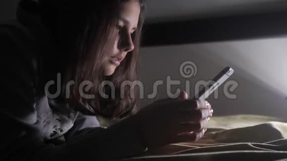 少女和智能手机晚上一个小少女在社交媒体上留言聊天视频的预览图