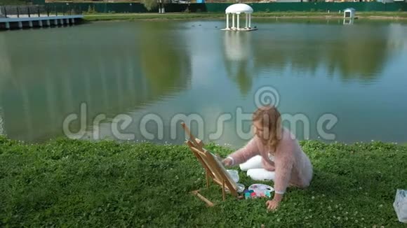 一个红头发的漂亮女人在画架上的画布上画了一幅画这位女士在附近的露天视频的预览图