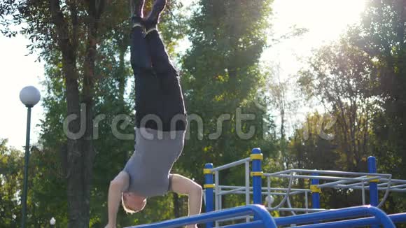 强壮的肌肉男在公园里做倒立适合肌肉发达的男性健身者在户外的横杠上做特技视频的预览图