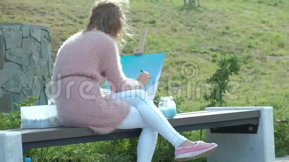 一个红头发的漂亮女人在画架上的画布上画了一幅画这位女士在附近的露天视频的预览图