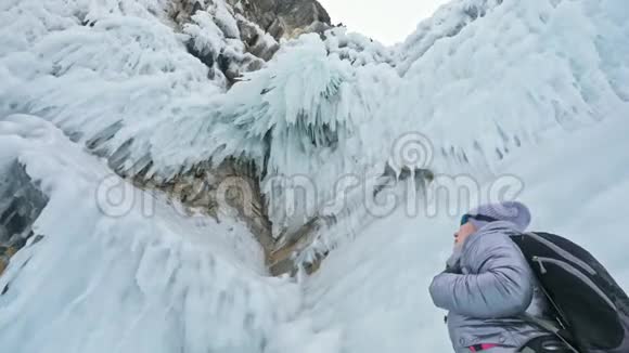 贝加尔湖冰上女子旅行去冬岛旅行女孩走在冰岩脚下旅行者看着视频的预览图