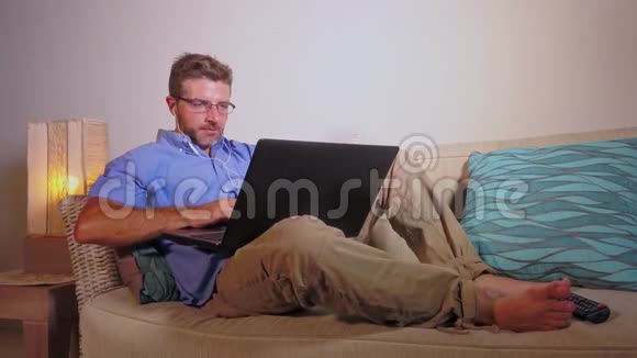 年轻快乐有魅力的企业家一个在家拿着笔记本电脑坐在现代公寓沙发上工作的年轻人视频的预览图