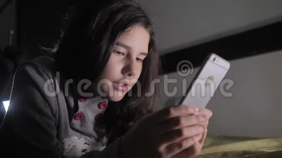 十几岁的女孩晚上在床上看她的智能手机一个小女孩在社交中写了一条聊天信息视频的预览图