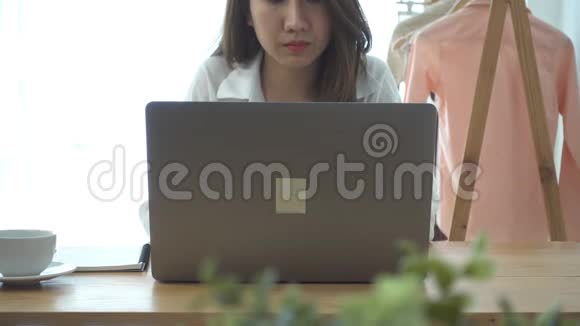 美丽的年轻微笑的女人在笔记本电脑上工作一边享受着温暖的咖啡坐在家里的客厅里视频的预览图