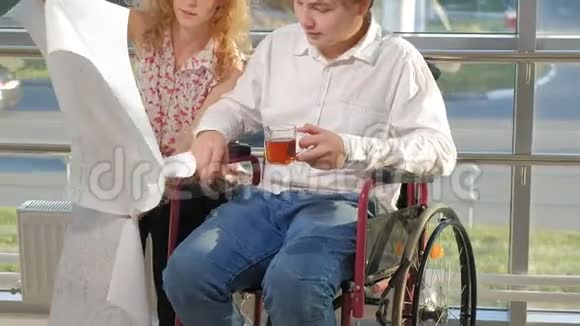 一位坐在轮椅上的残疾商人在窗户上一张大纸上写着一张照片与一位同事讨论工作视频的预览图