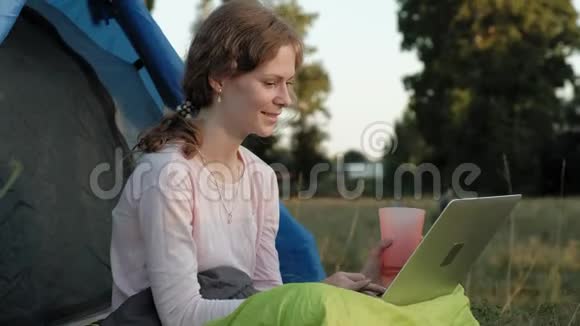 年轻女子在旧桥附近的旅游帐篷里的笔记本电脑后面工作视频的预览图