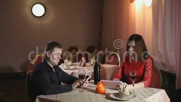 男人和女孩带着智能手机和平板电脑在咖啡馆浪漫的夜晚视频的预览图